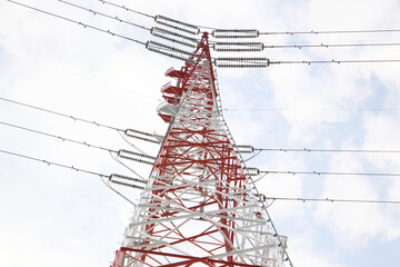 Red and white high-voltage transmission tower in Japan against a cloudy sky.