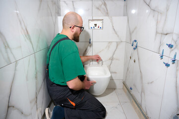 Plumber installing toilet. Modern toilet installation. Worker installing a wall-hung toilet on the...