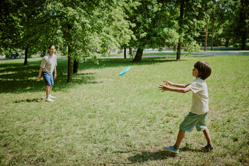 Asian father playing frisbee with child boy in green park, both smiling and enjoying outdoor activity together, trees and grass visible in background