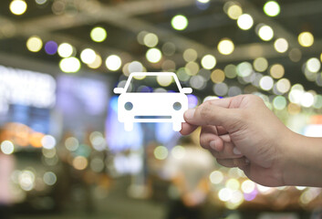 Hand holding car flat icon in fingers over blur light and shadow of shopping mall, Business transportation service concept