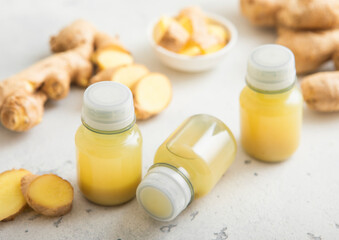 Ginger energy shot immune drink bottles with fresh raw ginger root on light background.Macro.
