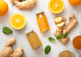 Bottles of immune ginger and orange energy shot drink with ginger root and turmeric powder on light background.Top view.