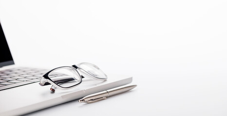 Closeup of an office table featuring a sleek laptop and reading glasses on a clean white surface