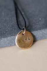Bronze Handcraft Soulful Amulet Pendant with Inspirational Word on Gray Stone Surface.
