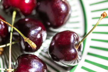 Macro closeup veiw of fresh red cherries with stems on a white plate with green stripes