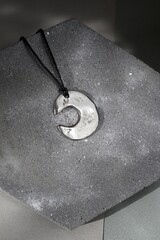 Silver Lunar Handmade Pendant on Textured Gray Background. Modern Jewelry Design. Stylish Accessory.