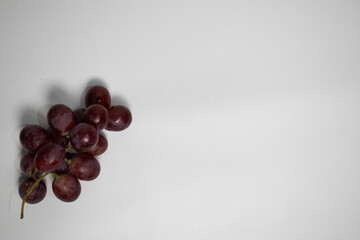 Minimalist top-down portrait of grapes placed on the left side of a plain background.