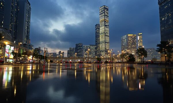 Cityscape reflection on wet pavement at night with tall buildings and cloudy sky backdrop scene
