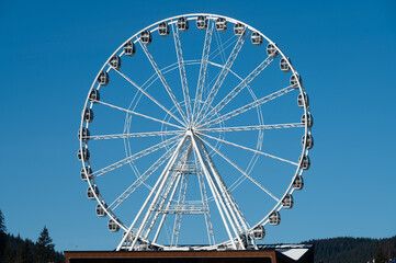 Giant observation wheel rotates against a clear blue sky in a bustling amusement park, offering...