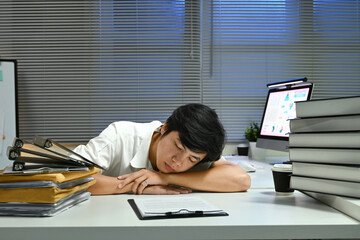 A man is sleeping on his desk with a stack of papers and a cup of coffee. The scene suggests that...