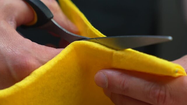 A man cuts a yellow kitchen rag with sharp scissors in a dark room.
A man with scissors in his hands and a yellow rag.
A rag in the hands of a man