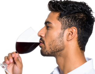 A young man with a beard and short hair is smelling a glass of red wine against a black background.