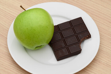 Green apple and bitten chocolate bar on a plate, sugar in food