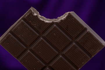 Close-up of a bitten dark chocolate cube in a bar