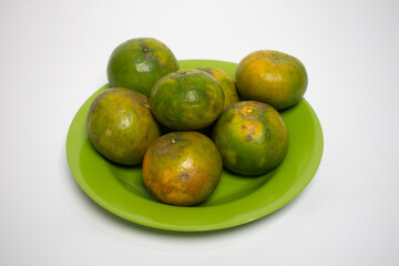 Green plate of ripe oranges, mostly green with a hint of yellow