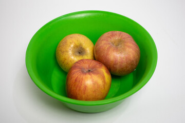 Three fresh apples in a bright green bowl on a white background.