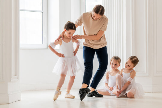 teaches young girl ballet in brightly colored studio, children watch.