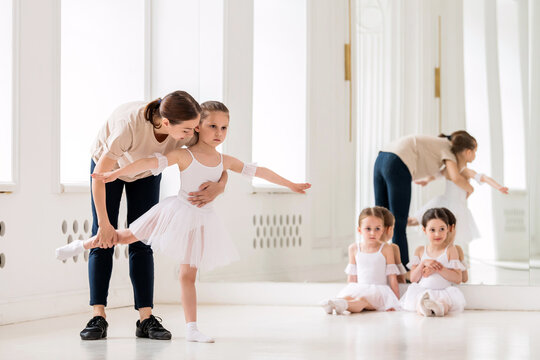 ballet teacher helps a girl in a white tutu perform an element
