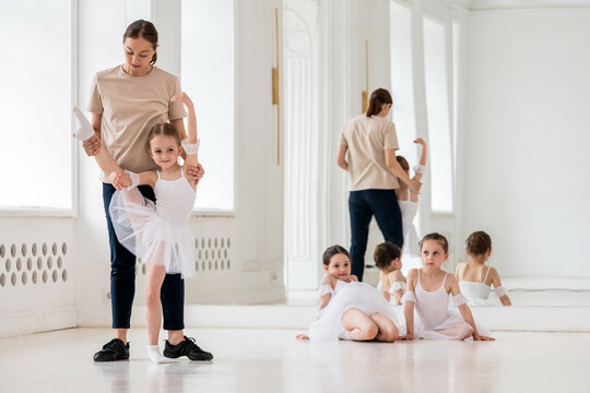 ballet teacher helps a girl in a white tutu perform an element