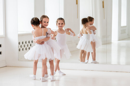 young girls in ballet tutus embracing and smiling in a bright studio - Powered by Adobe