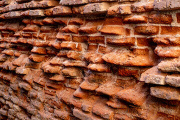 A close-up of a beat-up red brick wall with rough, uneven bricks in shades of red, orange, and brown, showing off years of wear and tear.