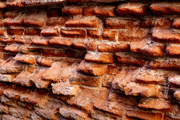 A close-up of a beat-up red brick wall with rough, uneven bricks in shades of red, orange, and...