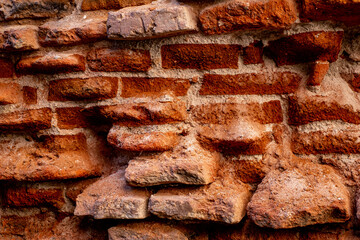 A close-up of a beat-up red brick wall with rough, uneven bricks in shades of red, orange, and...