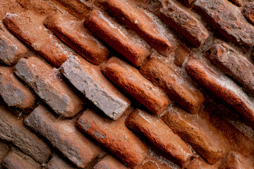 A close-up of a beat-up red brick wall with rough, uneven bricks in shades of red, orange, and brown, showing off years of wear and tear.