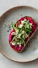 Close-up of elegant open-faced toast with beetroot hummus, feta crumbles, arugula and cracked pepper