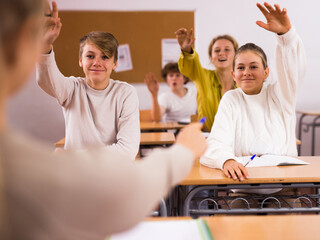 Teenage schoolboys and schoolgirls sitting with hands raised during lesson at secondary school