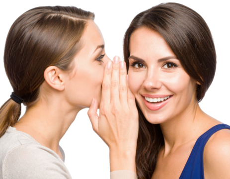 Two women, one whispering a secret to the other, who smiles brightly against a black background.