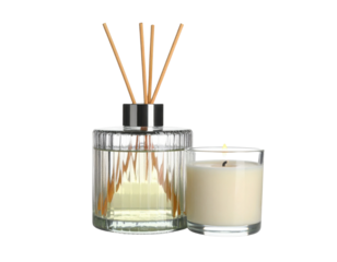 A glass reed diffuser with wooden sticks and a lit white candle in a glass holder.
