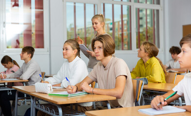 Group of diligent school kids and teacher during lesson in classroom in secondary school