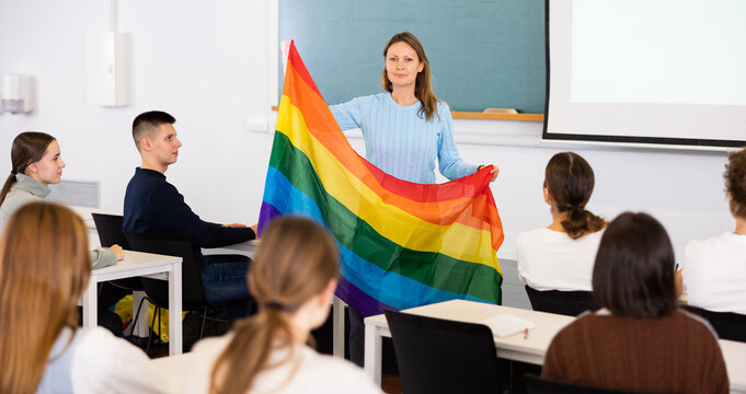 Adult female teacher in classroom showing LGBT flag to students in class