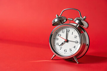 Silver alarm clock with bells stands on a red surface showing the time