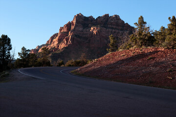 A lonely mountain at sunset. An American highway turns around the mountain. Coniferous trees are...