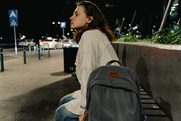 Sad young woman waiting for bus in night city at bus stop