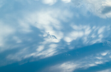 Soft, wispy stratocumulus clouds spread across a pale blue sky, with gentle shading creating a