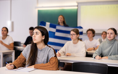 Students study in classroom, teacher stands behind with flag of Greece
