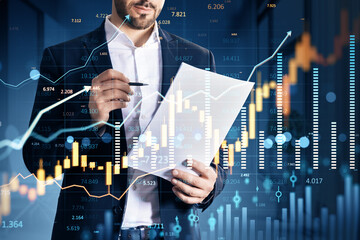 Businessman analyzing financial charts on paper with digital market data graphics overlay in modern fintech environment background..
