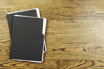 Black document folders with white papers on brown wooden desk, top view with empty space for text...