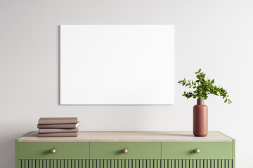 Blank white canvas on wall above green wooden dresser with books and flower vase in modern interior...