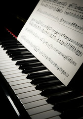 Fototapeta premium Piano keyboard with sheet music placed on top. Detailed view of the keys and musical notes. Professional musician in a classical music setting. Studio.