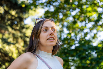 Close-up portrait of smiling woman with sunglasses on head in park setting, surrounded by trees and...