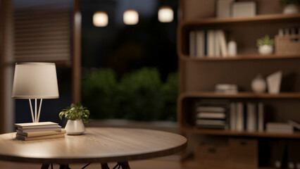 Books under lamp on round wooden table with blurred background of a living room or bedroom at night.