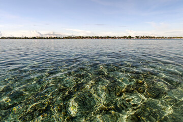 Crystal-clear turquoise waters with coral reef visible beneath the surface, with the coastline of Semporna, Sabah in the background.
