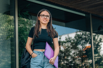 teenage girl student in front of school with folder and backpack