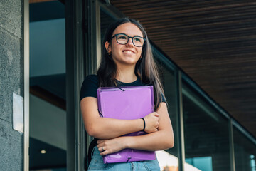 teenage girl student in front of school with folder and backpack