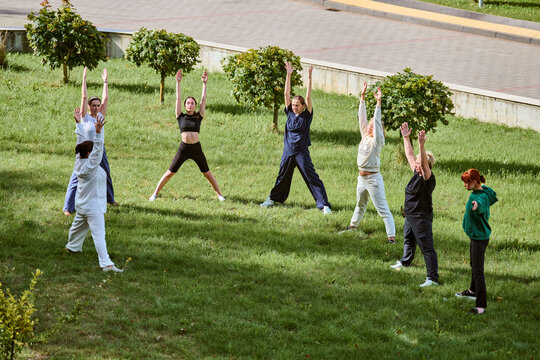Group of adults practicing qigong in grassy park. Sunny day enhances natures vibrant colors. Participants include men and women, displaying relaxed, focused expressions - Powered by Adobe