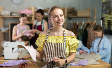 Positive teen girl child in study room of sewing school and young designers. Group of students in background during discussion of work processes